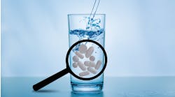 Glass of water with magnifying glass showing presence of pharmaceuticals in water