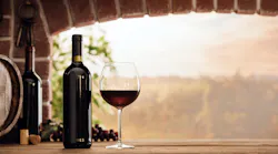 wineglass and bottles next to the window and panoramic view of vineyards at sunset