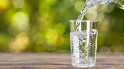 water from jug pouring into glass on wooden table outdoors