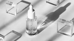 Serum cosmetic bottle mockup on acrylic transparent solid block pedestal on white background, shadow from sun, natural light from windows.