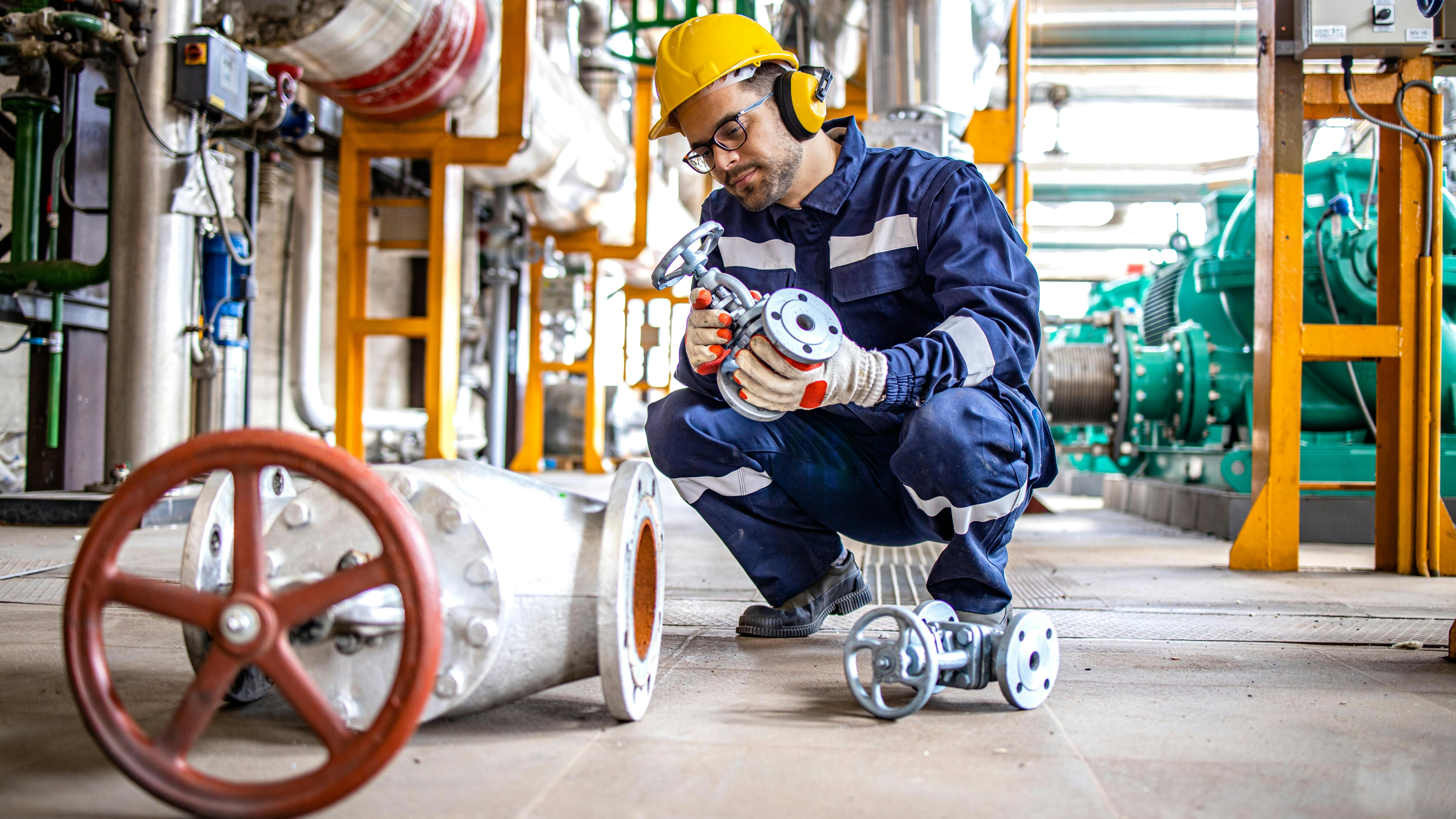 Hardworking industrial technician inspecting high pressure valve inside refinery plant.