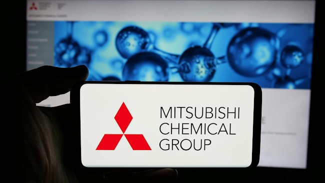 Person holding cellphone with logo of company Mitsubishi Chemical Group Corporation on screen in front of business webpage. Focus on phone display.