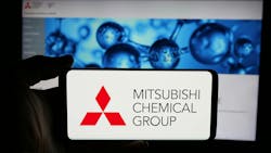 Person holding cellphone with logo of company Mitsubishi Chemical Group Corporation on screen in front of business webpage. Focus on phone display. Person holding cellphone with logo of company Mitsubishi Chemical Group Corporation on screen in front of business webpage. Focus on phone display.