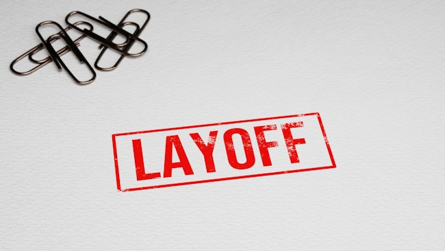 LAYOFF rubber stamp on paper with paper pins in the background.