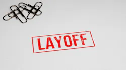 LAYOFF rubber stamp on paper with paper pins in the background.