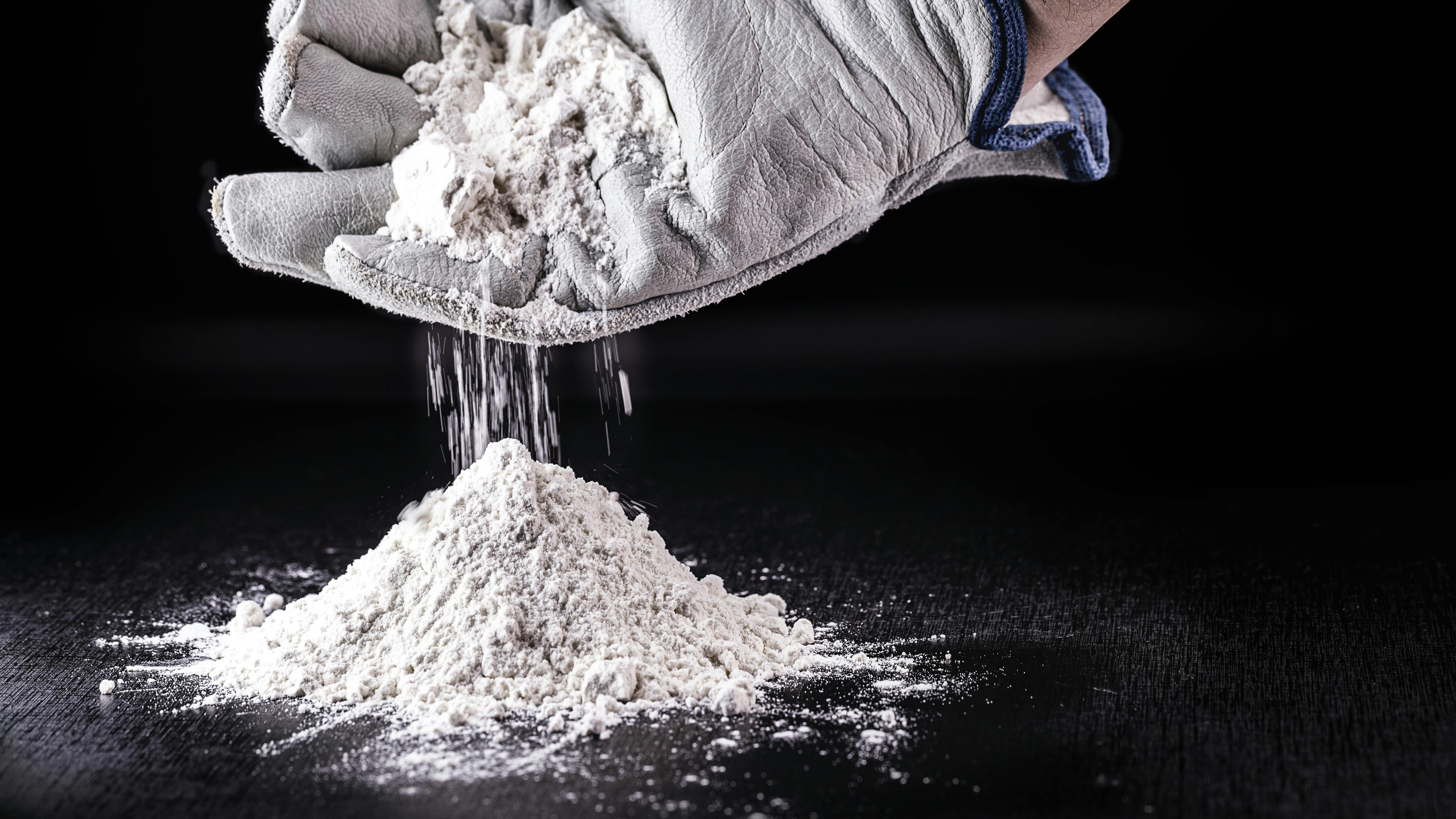 gloved hand cups white powder dropping it into a pile
