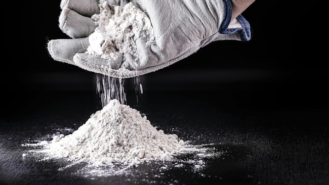 gloved hand cups white powder dropping it into a pile