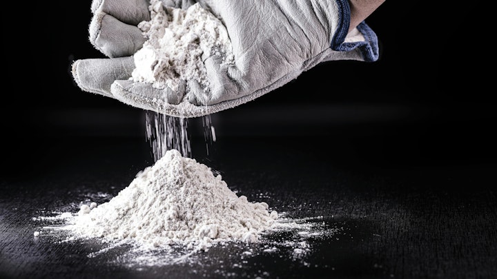 gloved hand cups white powder dropping it into a pile