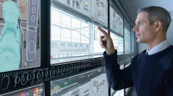 man stands in front of wall of computer screens and selects components on touchscreen