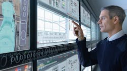 man stands in front of wall of computer screens and selects components on touchscreen man stands in front of wall of computer screens and selects components on touchscreen