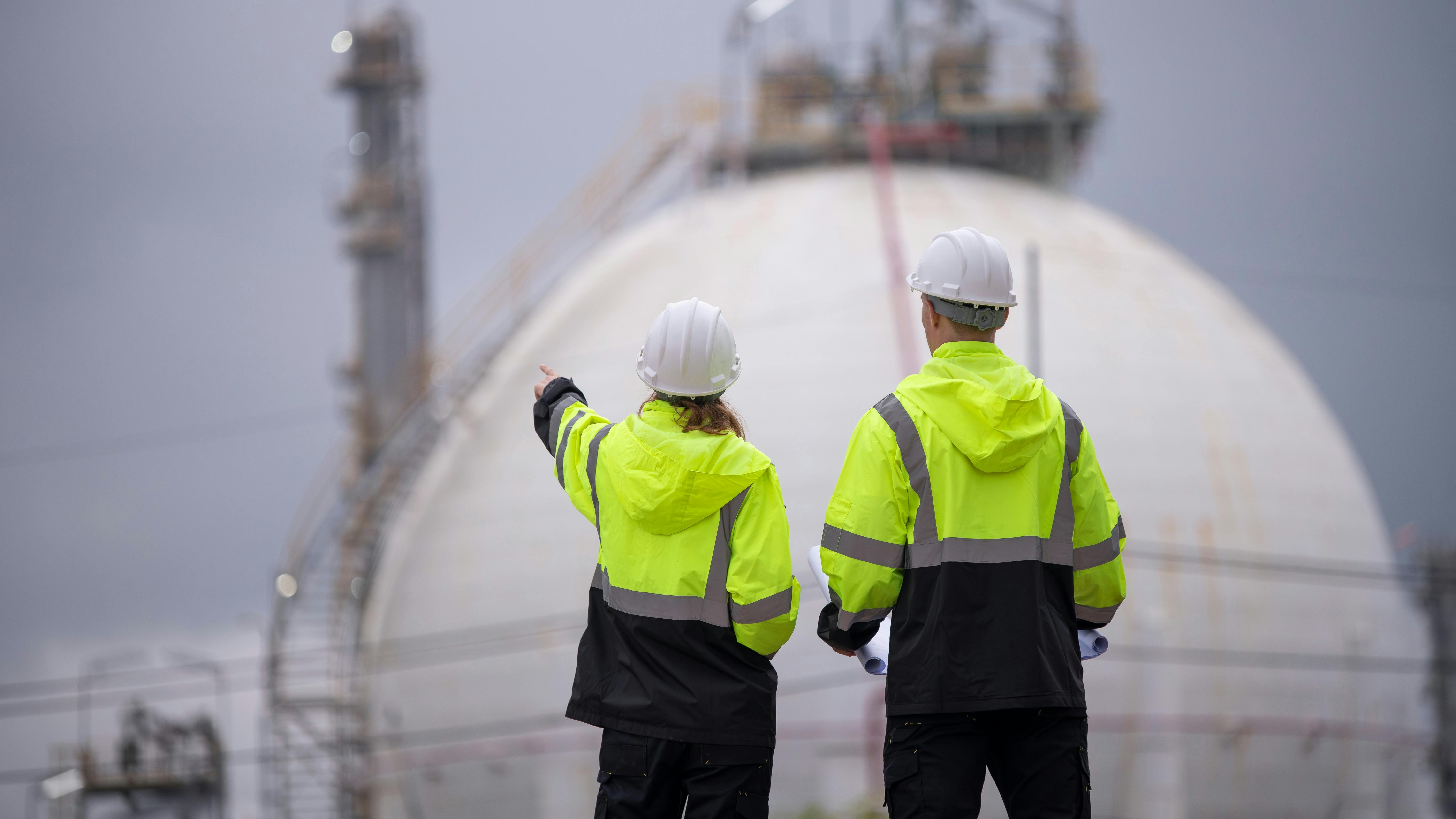 Engineers wearing safety gear, including hard hats with chemical plant in background