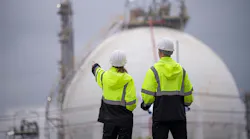 Engineers wearing safety gear, including hard hats with chemical plant in background