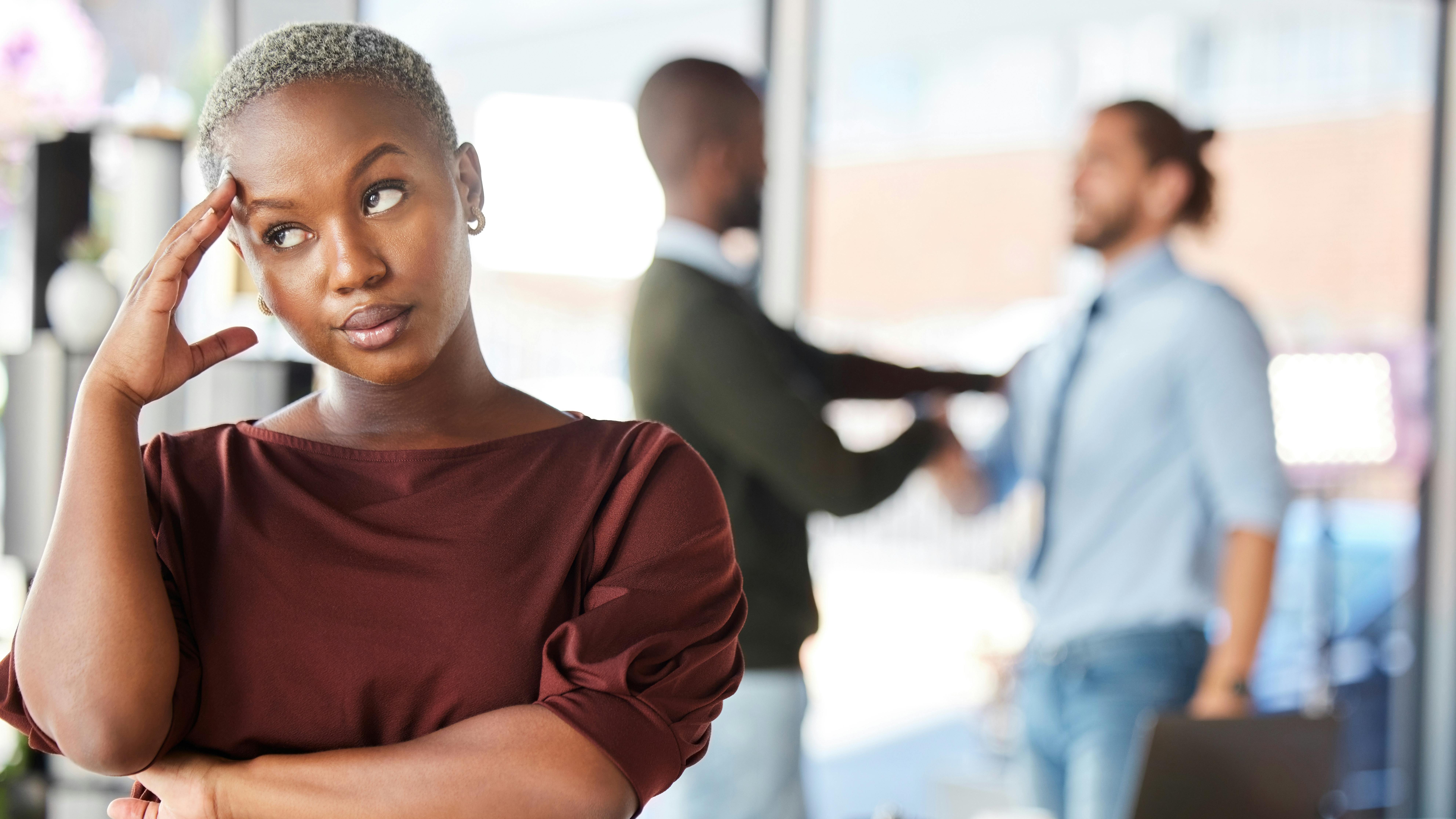 Woman rolls eyes as two men in the background who are friendlier to each other indicate possible sexism and discrimination
