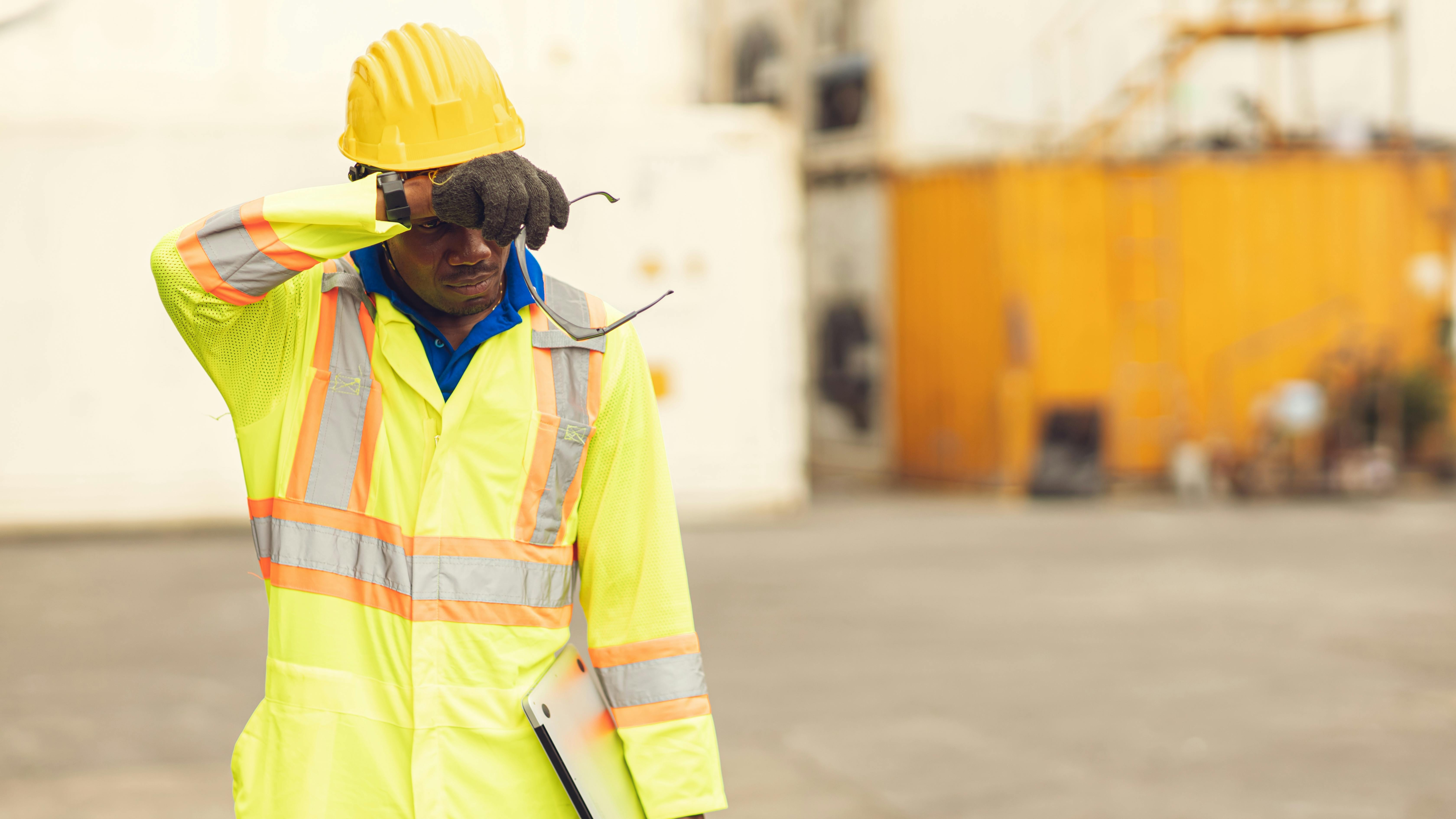 African American worker in safety apparely and hard hat, wiping brow to combat sweat and heat