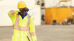 African American worker in safety apparely and hard hat, wiping brow to combat sweat and heat
