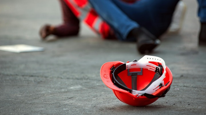 Workplace Safety red helmet on ground with fallen worker in background