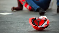 Workplace Safety red helmet on ground with fallen worker in background