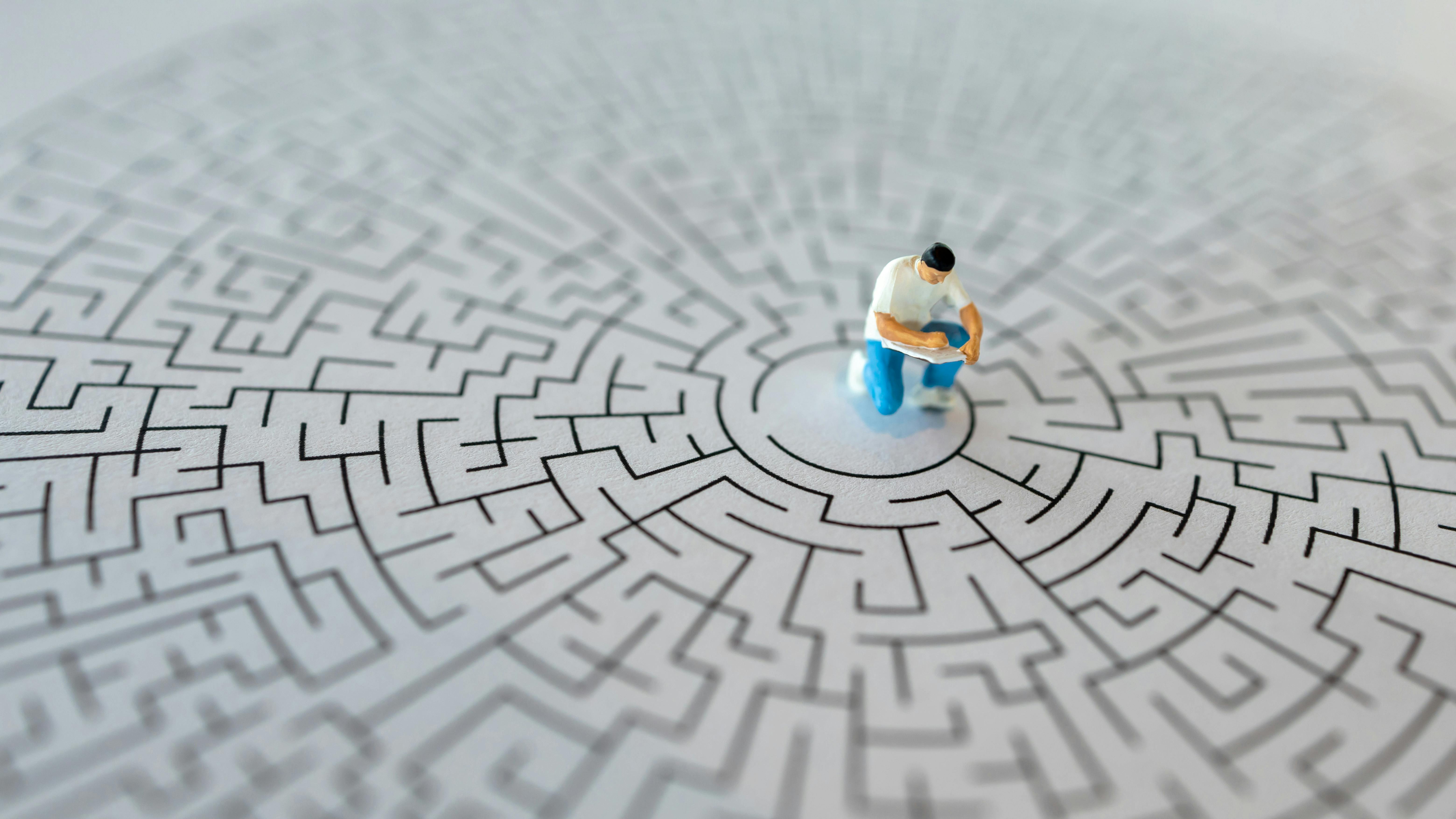 Miniature figurine of man writing in book sits in center of a maze, concept of troubleshooting