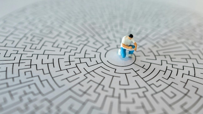 Miniature figurine of man writing in book sits in center of a maze, concept of troubleshooting
