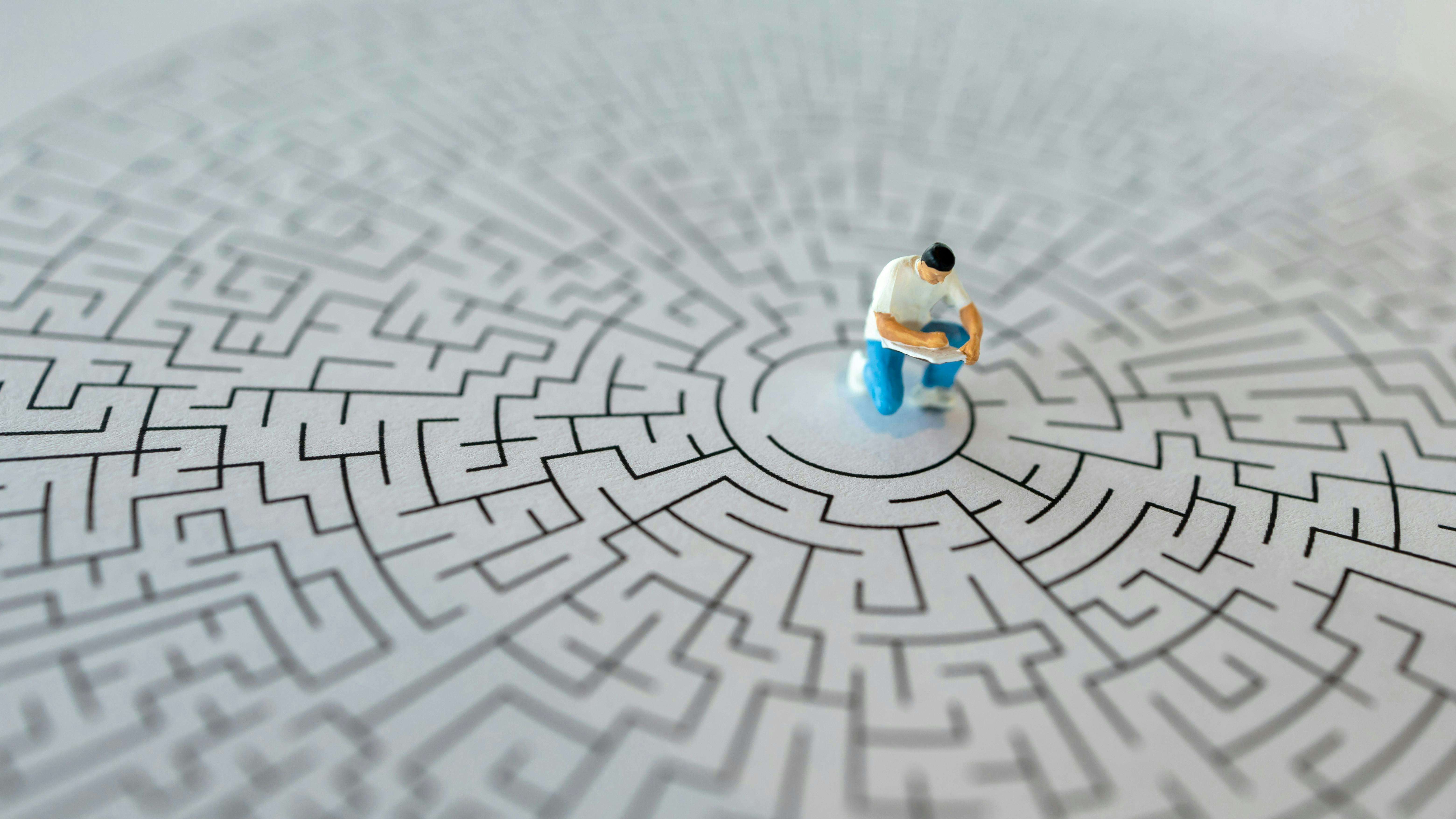 Miniature figurine of man writing in book sits in center of a maze, concept of troubleshooting