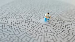 Miniature figurine of man writing in book sits in center of a maze, concept of troubleshooting Miniature figurine of man writing in book sits in center of a maze, concept of troubleshooting