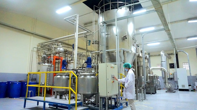 A male operator stands in front of a control panel of a spray dryer machine made of stainless steel in a food factory
