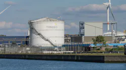 Industrial view of the Trinseo chemical plant with storage tank, wind turbines, and canal water in the foreground under a partly cloudy blue sky. Tessenderlo-Ham, Belgium