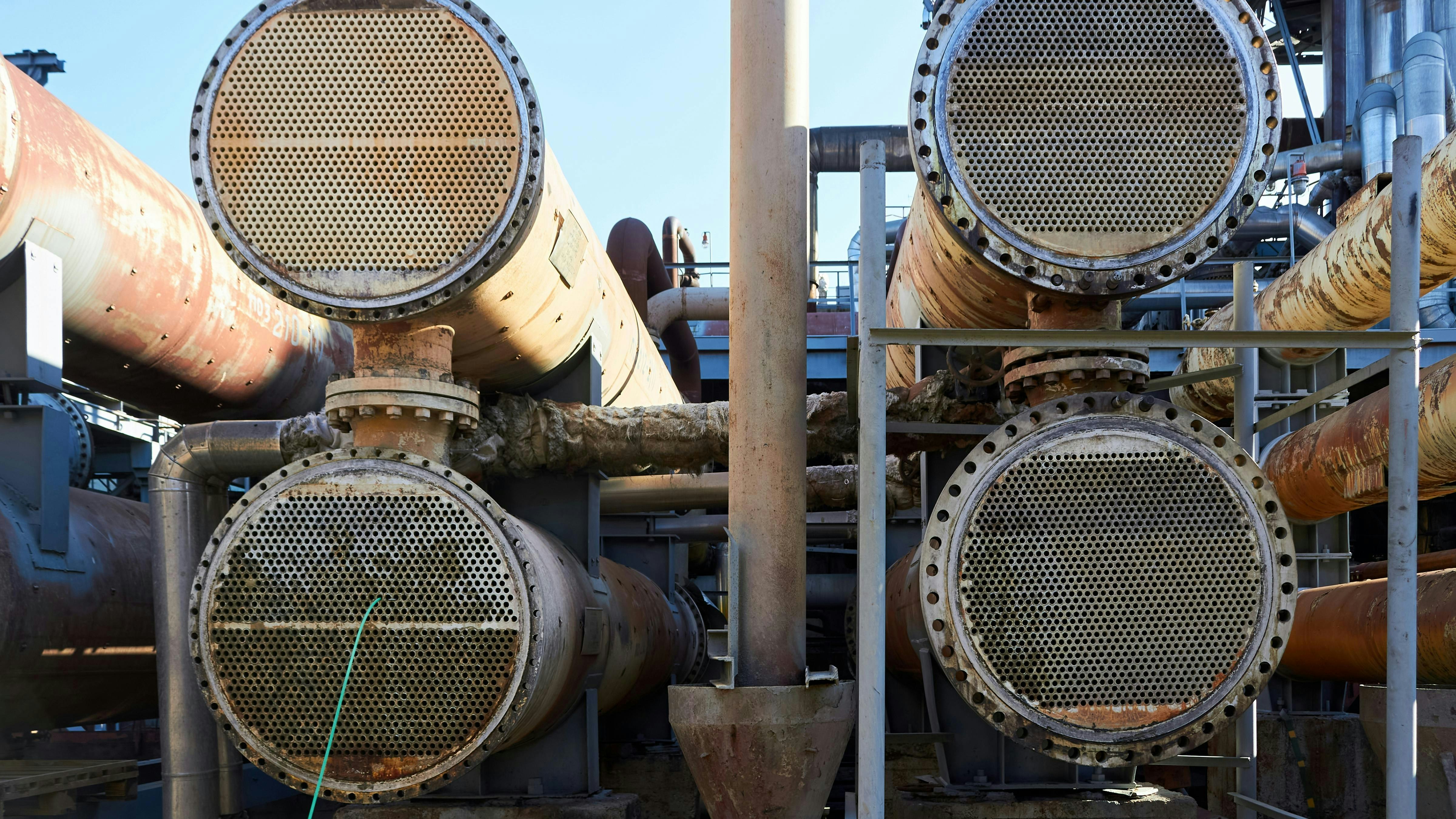 Four Two way heat exchangers shell and tubes opened for repairing and deposits cleaning with high-pressure hydraulic unit.