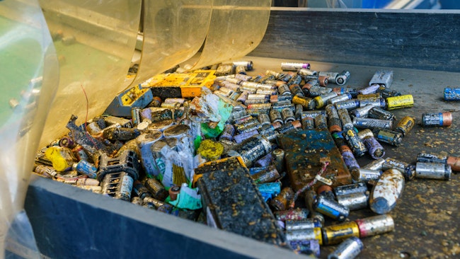 Industrial battery recycling process with conveyor belts filled with old batteries, barrels of discarded batteries, disassembled car batteries and sorted raw material