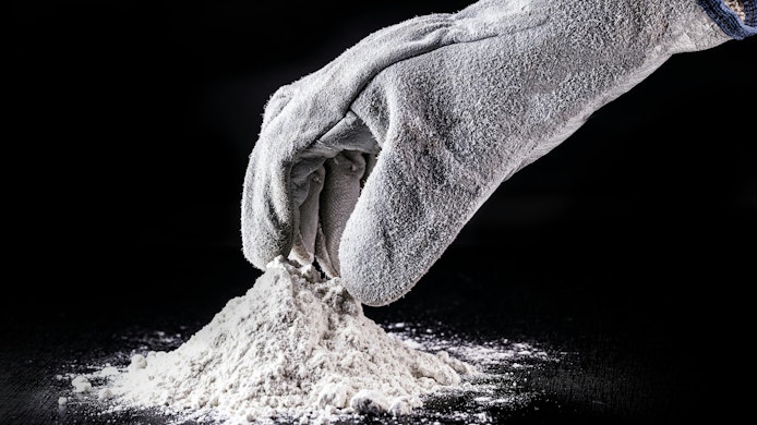 gloved hand reaches into small pile of powder surrounded by black background