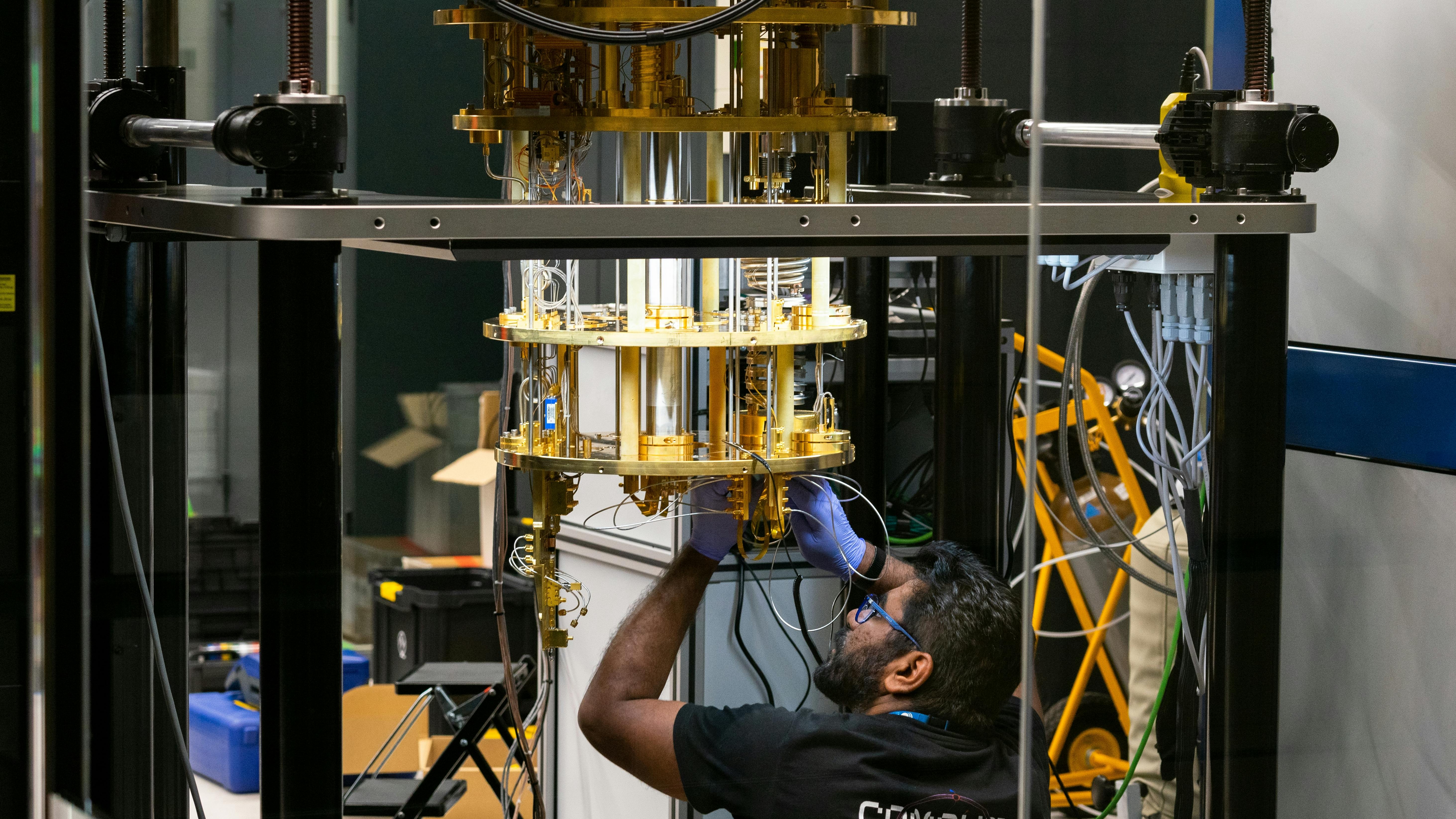 Engineer operating advanced quantum computing equipment through glass in research lab with cryogenic cooling and braided tubing.