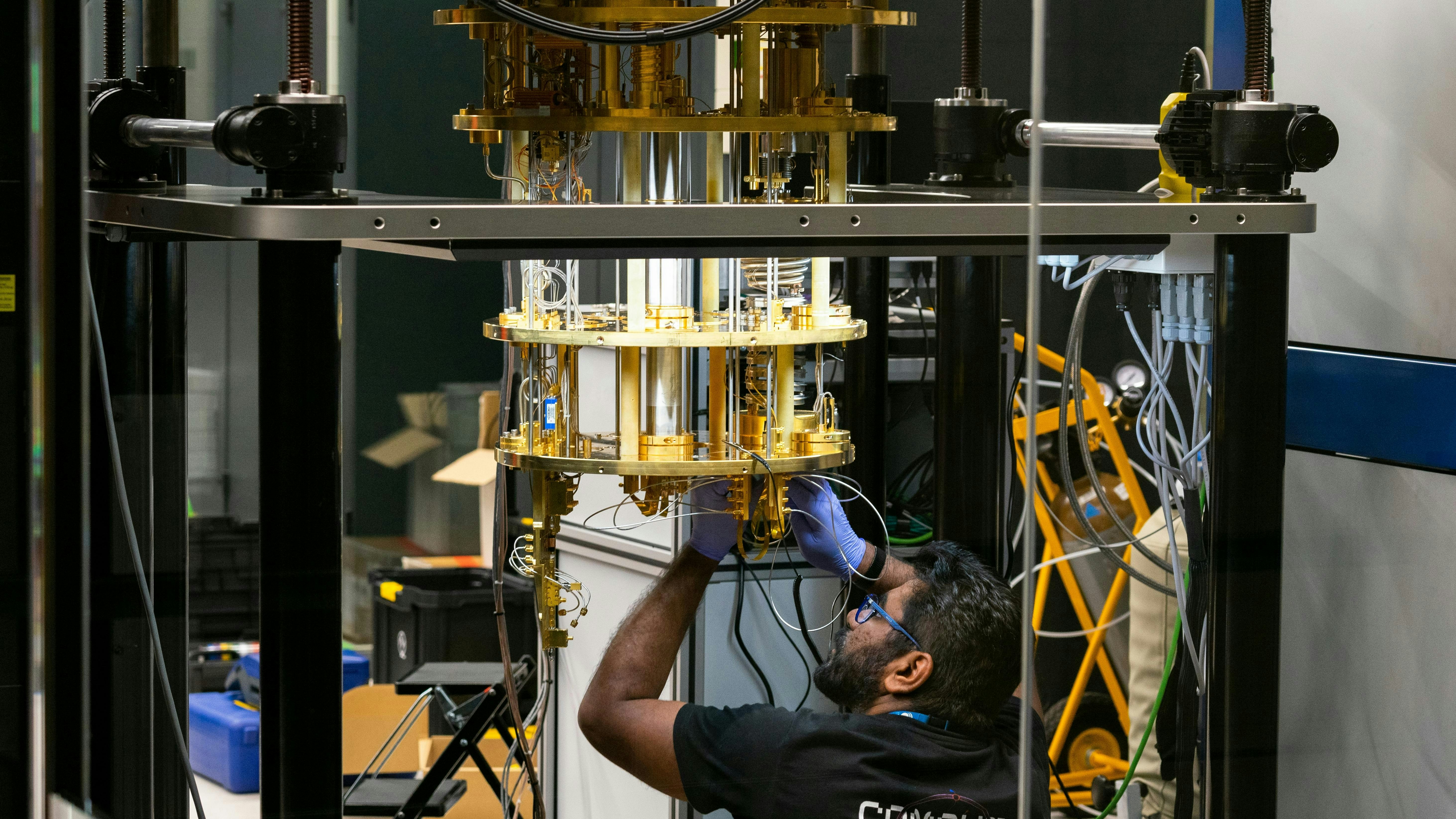 Engineer operating advanced quantum computing equipment through glass in research lab with cryogenic cooling and braided tubing.