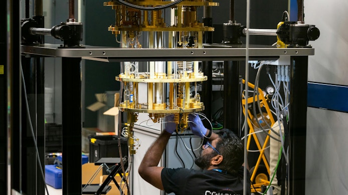 Engineer operating advanced quantum computing equipment through glass in research lab with cryogenic cooling and braided tubing.