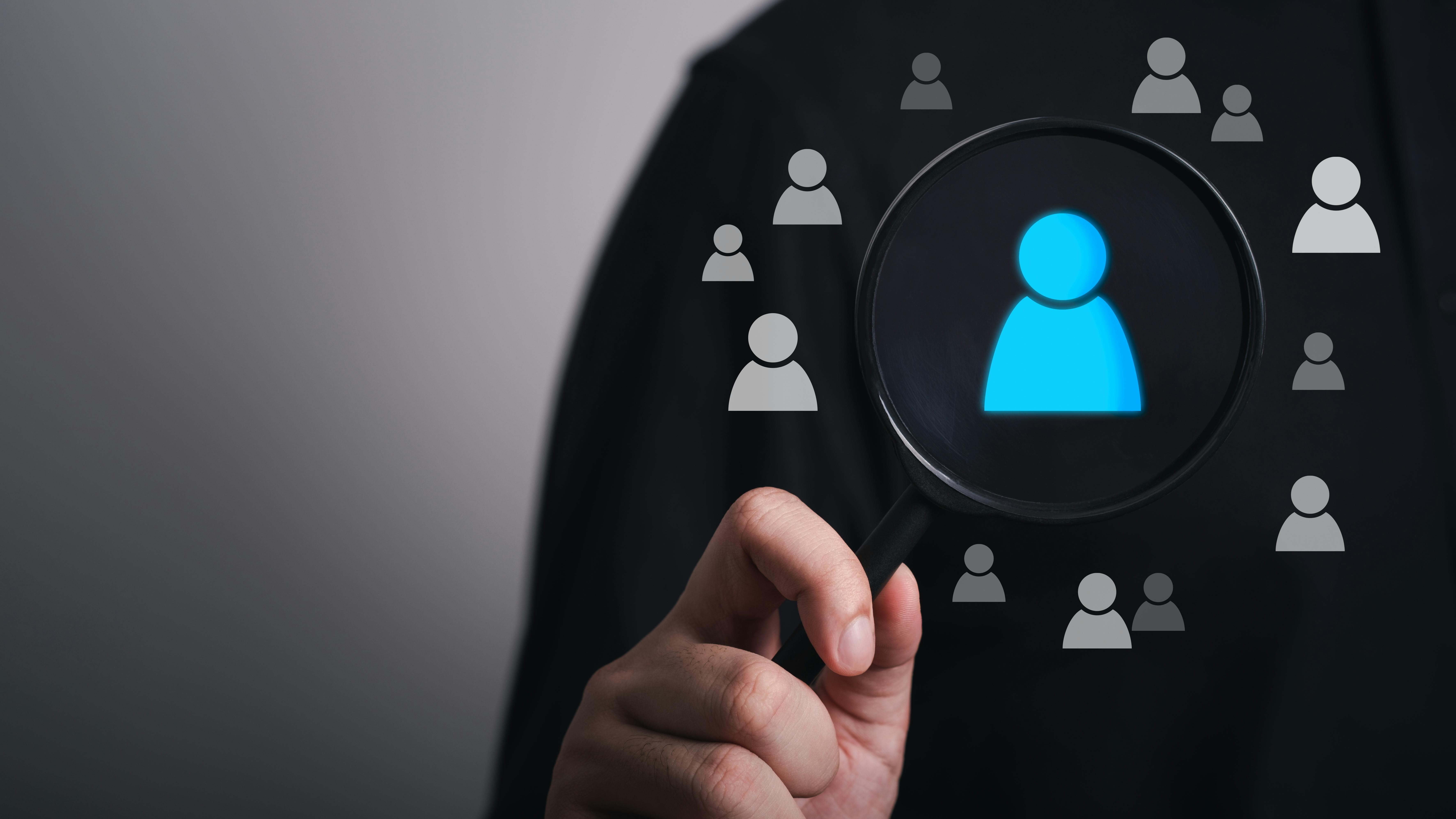 Hand holding Magnifier glass focused on executive search of personnel icons