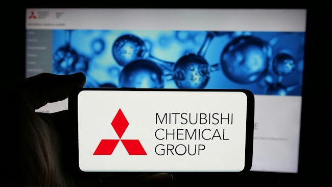 Mitsubishi Chemical Group logo displayed on phone screen with company website on computer screen in background