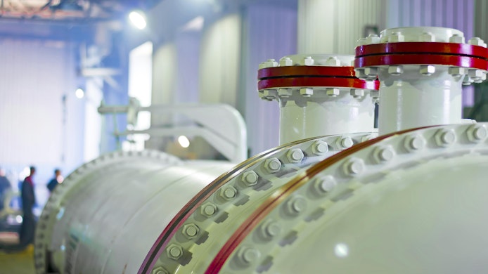 closeup shot of heat exchanger inside plant with people walking in background