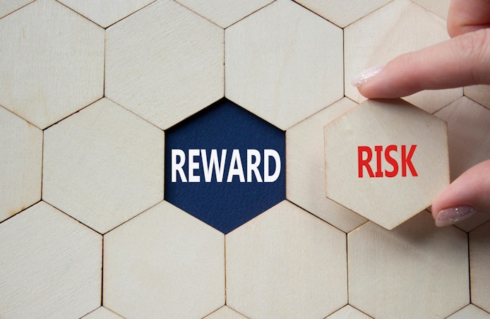 hand holds a hexagonal tile with the word risk. in the background hexagonal tiles surround empty slot that reveals the word reward