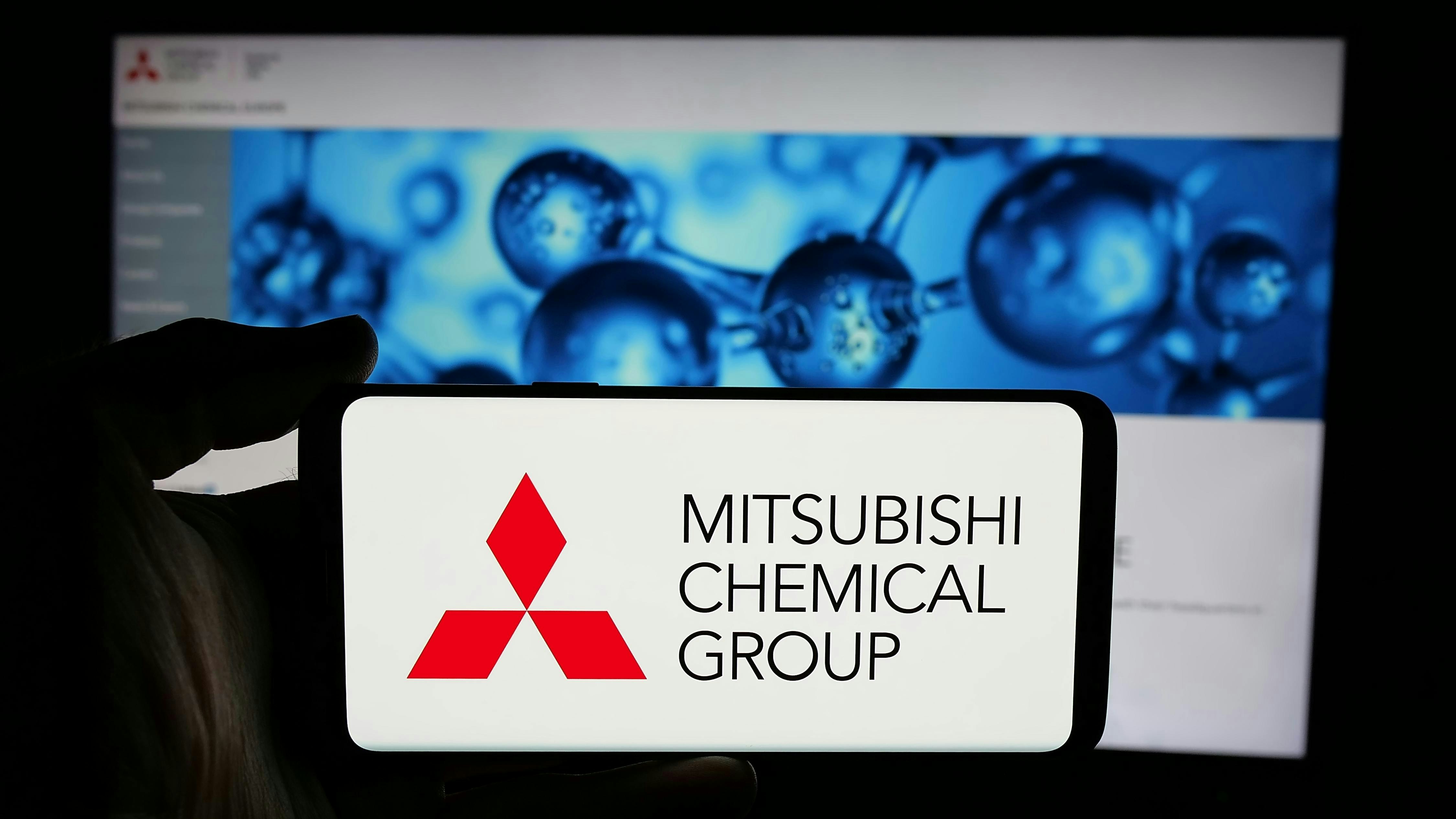 Person holding cellphone with logo of company Mitsubishi Chemical Group Corporation on screen in front of business webpage.