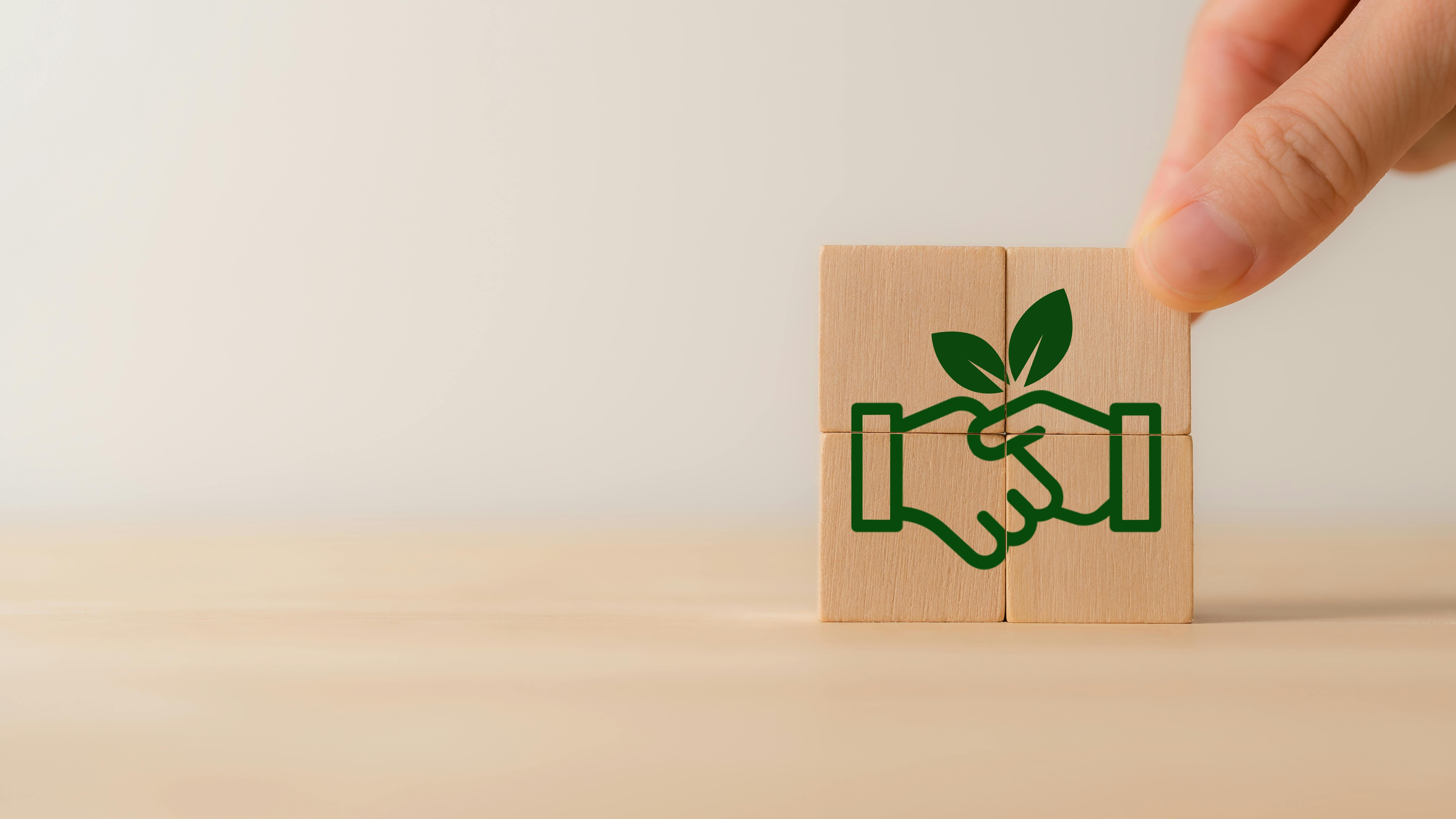 Four wooden blocks stacked together to reveal image of handshake with a green leaf included