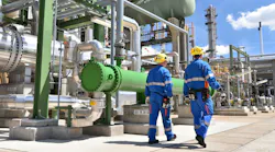 2 workers walking around outside of petrochemical plant with pipes and valves in background
