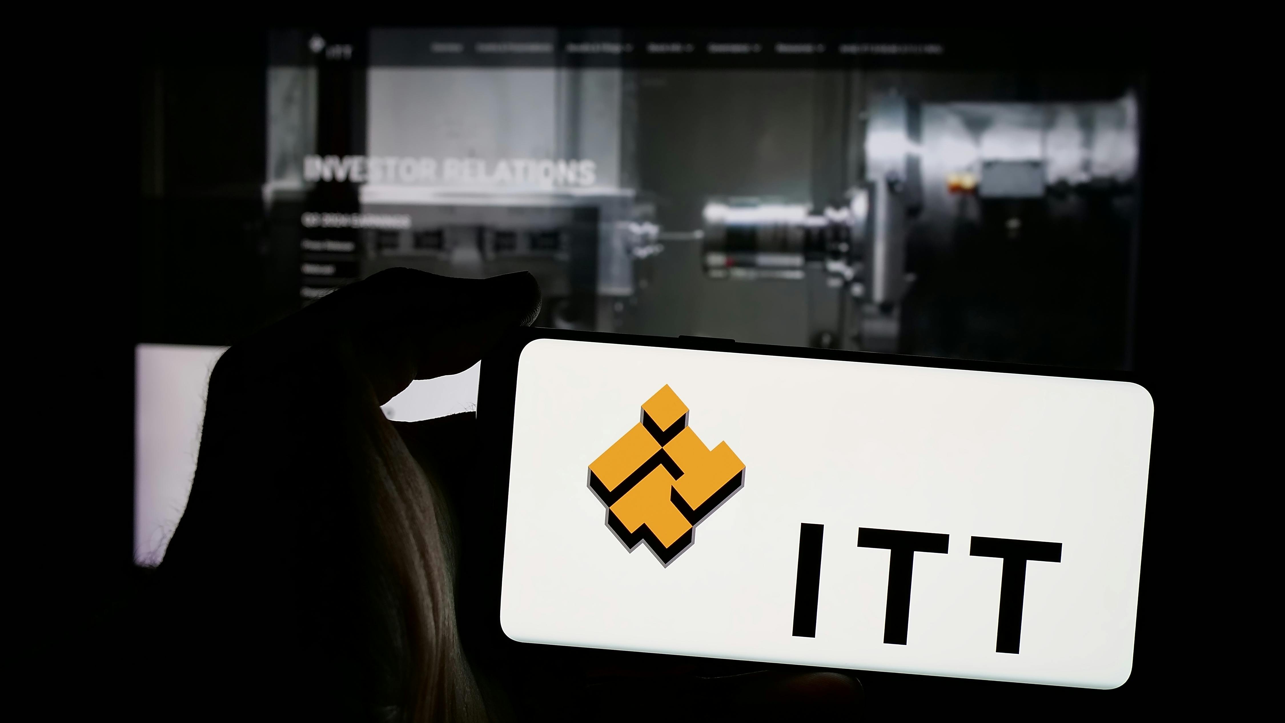 Person holding mobile phone with logo of American industrial manufacturing company ITT Inc. on screen in front of web page. Focus on phone display. Unmodified photo.