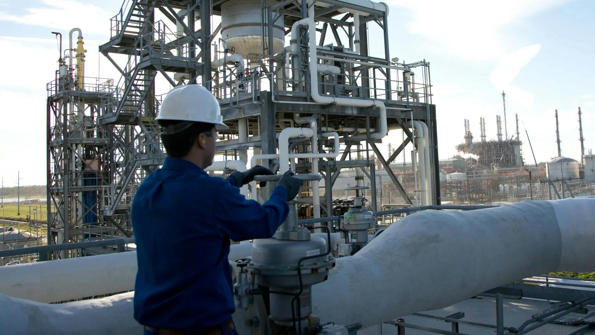 Industrial worker in blue coveralls and white hard hat operating a valve at Shintech Louisiana site
