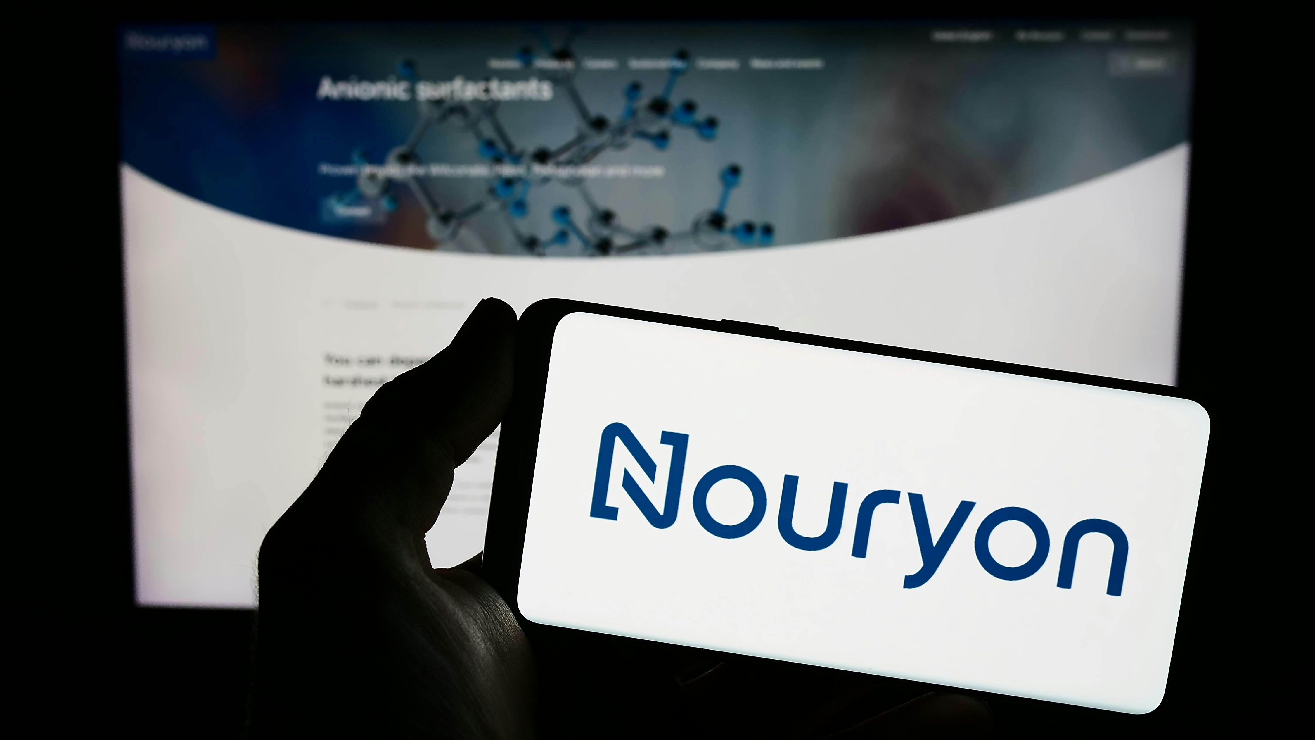 erson holding smartphone with logo of Dutch company Nouryon Chemicals Holding B.V. on screen in front of website.