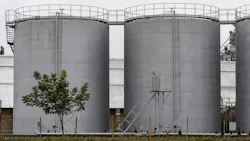 Several large fuel storage tanks stand at an industrial site, surrounded by a few trees and equipment, reflecting an overcast atmosphere in the morning light Several large fuel storage tanks stand at an industrial site, surrounded by a few trees and equipment, reflecting an overcast atmosphere in the morning light