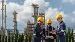 3 workers in safety gear with oil and gas refinery plant in background 3 workers in safety gear with oil and gas refinery plant in background