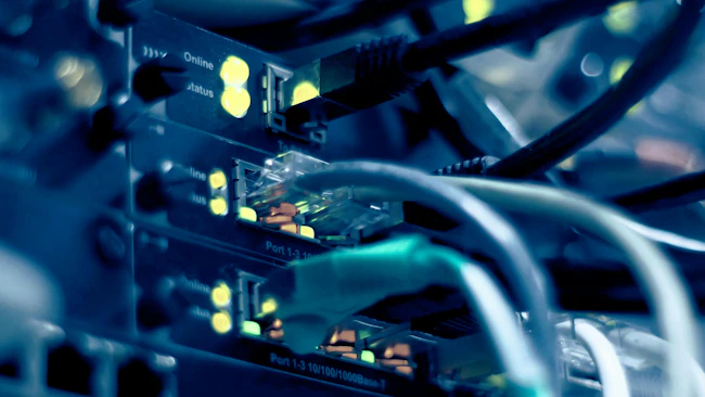 Close-up of network switch ports with ethernet cables and glowing yellow status indicator lights.