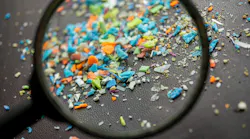 A magnifying glass examining colorful microplastic particles scattered on a dark surface. A magnifying glass examining colorful microplastic particles scattered on a dark surface.