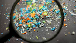 A magnifying glass examining colorful microplastic particles scattered on a dark surface. A magnifying glass examining colorful microplastic particles scattered on a dark surface.