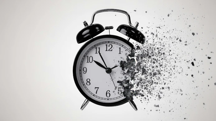 Striking monochrome image of a classic black alarm clock in the process of dissolving into a cloud of dark, gritty particles.