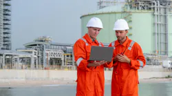 Two engineers in orange coveralls and hard hats review a laptop at an industrial waterfront facility. Two engineers in orange coveralls and hard hats review a laptop at an industrial waterfront facility.